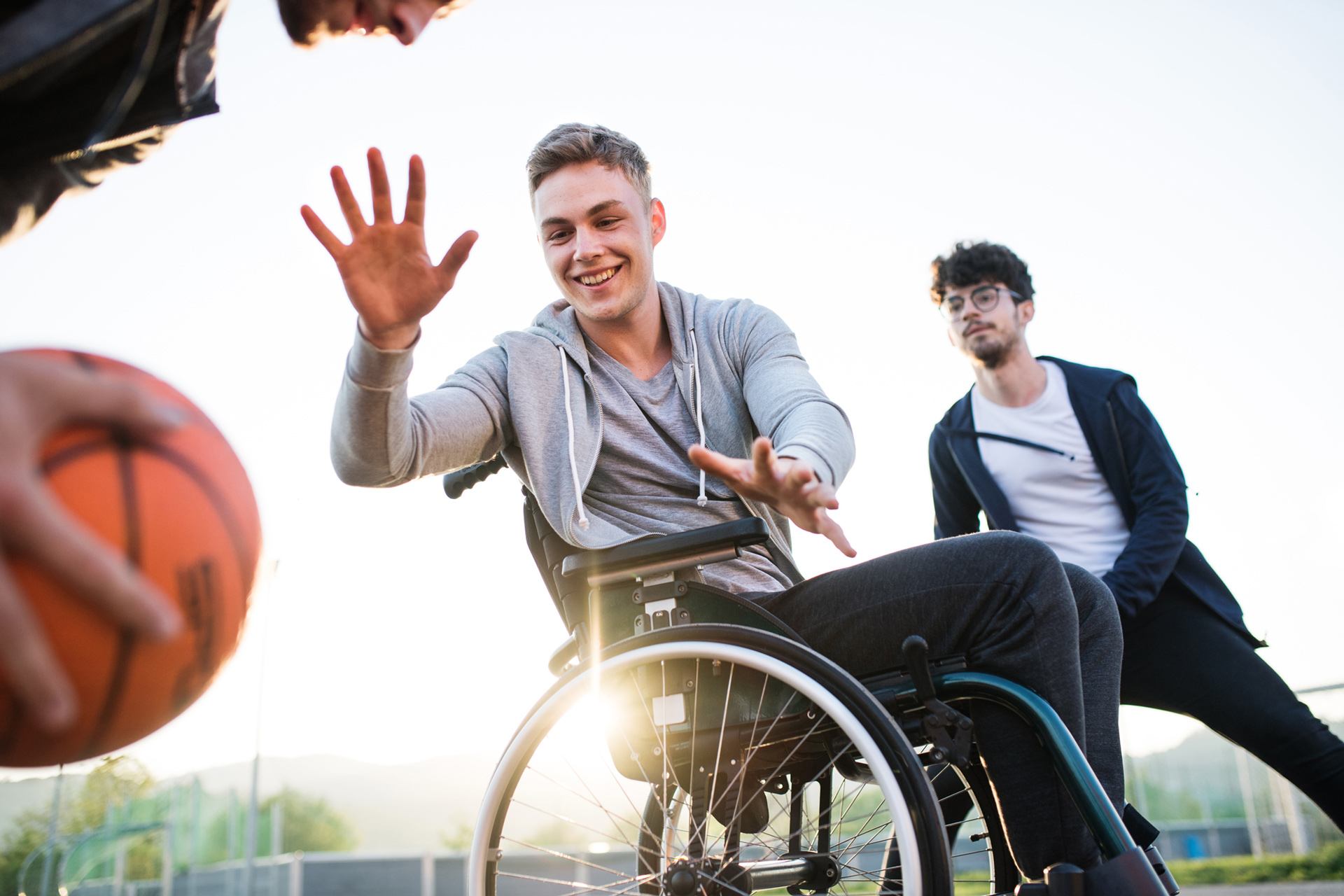 3 Basketballspieler spielen Basketball. Einer der Spieler ist Rollstuhlfahrer und versucht einem Spieler den Ball abzunehmen